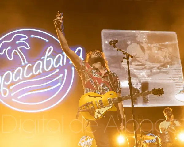 El cantante de Izal en Albacete levanta la mano con su guitarra amarilla, iluminado por un neón de Copacabana.