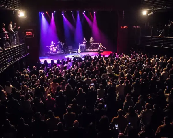 Un concierto en Guitar BCN ilumina el escenario con luces púrpuras mientras una multitud entusiasta graba el momento.