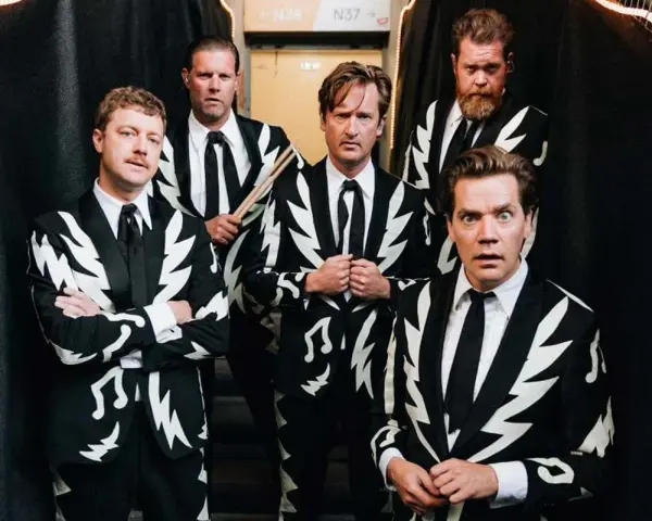 Los miembros de The Hives posan con trajes llamativos. Uno sostiene baquetas, listo para la acción.