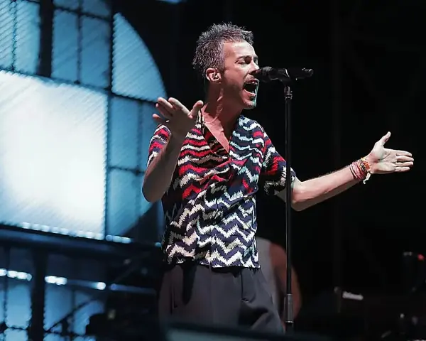 El cantante de Vetusta Morla Sevilla canta apasionadamente en un concierto, con las manos extendidas y un micrófono frente a él.