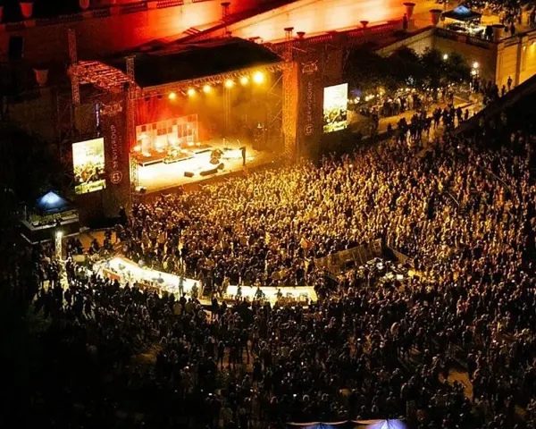 Multitudinaria asistencia a conciertos en julio. Una banda toca en un escenario iluminado ante miles de fans.