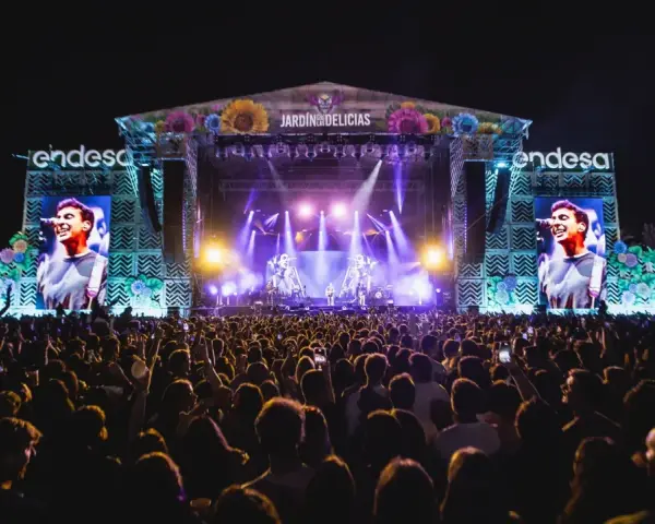 Gran concierto en el Jardín de las Delicias. Multitud vibrante ante el escenario iluminado, con pantallas gigantes mostrando al artista.