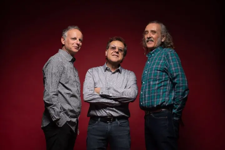 Los miembros de Els Pets posan sonrientes ante un fondo rojo.