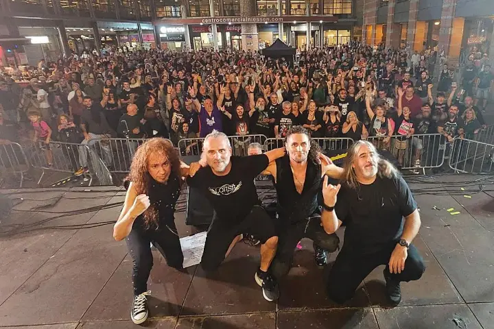 La banda Syberia posa con su público. Los músicos, con atuendos oscuros, se arrodillan mientras una multitud enardecida los aclama.