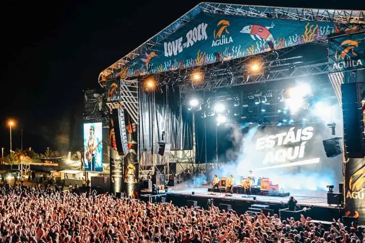 Multitud en concierto, luces brillantes y humo en el escenario. El cartel dice "Love to Rock".