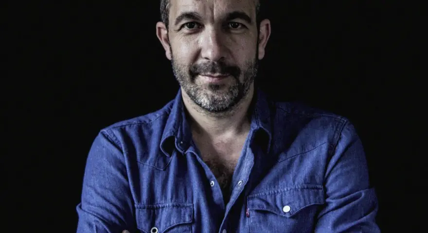 Hombre con barba y camisa vaquera azul, mirada directa. Podría ser DJ Coco listo para pinchar.