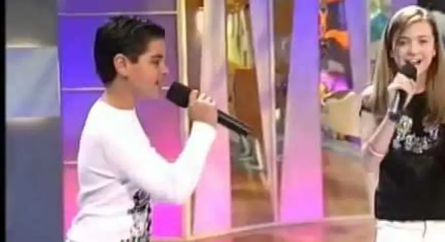 Ana Mena y Abraham Mateo, de niños, cantando con micrófonos en un escenario.