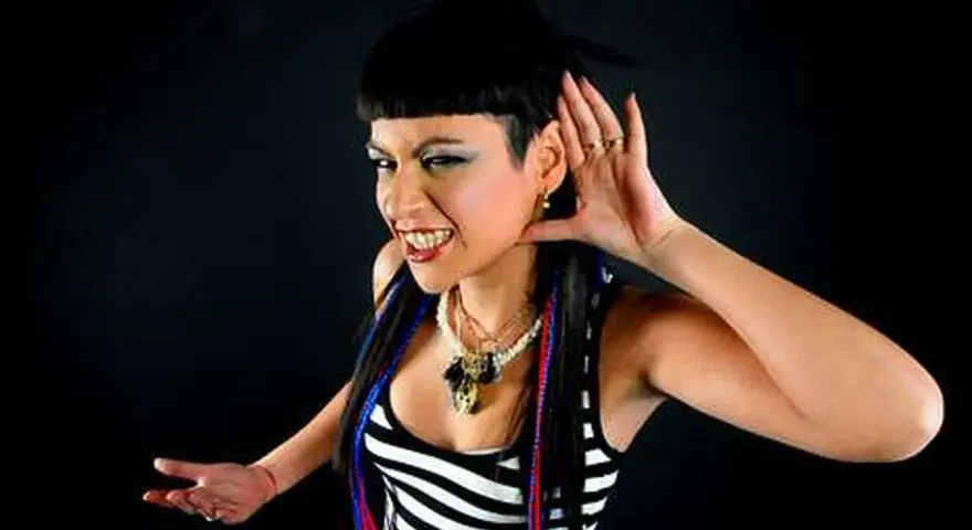 Fatima Hajji, con su característico estilo, escucha atentamente, con una mano en la oreja y una sonrisa pícara.