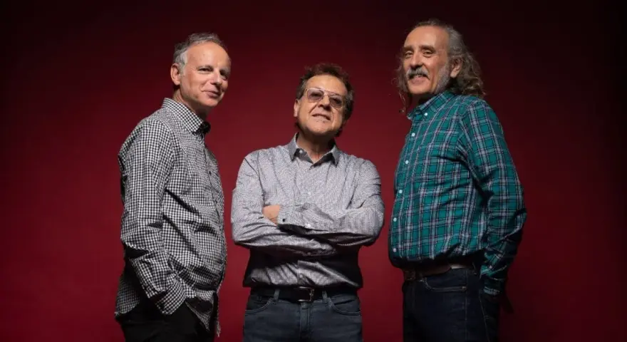 Los miembros de Els Pets posan sonrientes ante un fondo rojo.