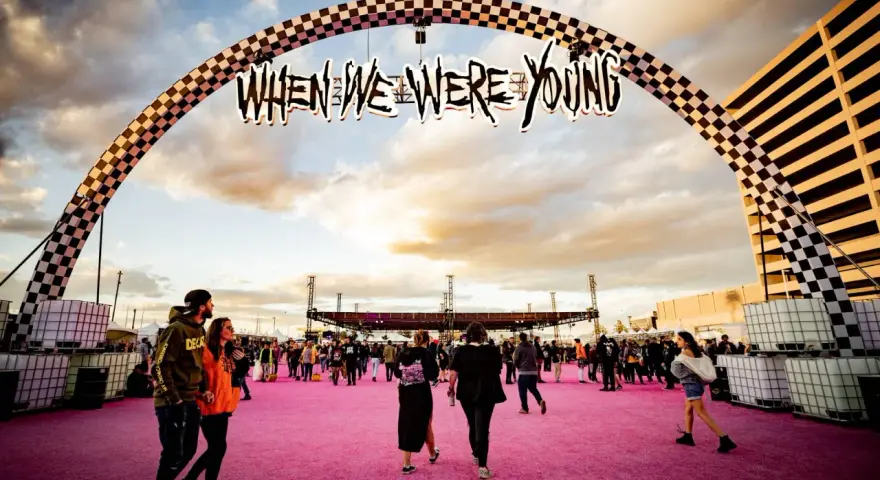 Gente camina bajo un arco con el letrero "When We Were Young Festival" sobre una alfombra rosa.