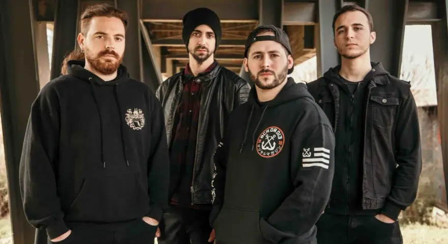 Cuatro hombres con sudaderas y chaquetas negras posan bajo una estructura metálica. Sus miradas intensas parecen **blaze out** con determinación.
