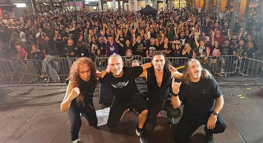 La banda Syberia posa con su público. Los músicos, con atuendos oscuros, se arrodillan mientras una multitud enardecida los aclama.