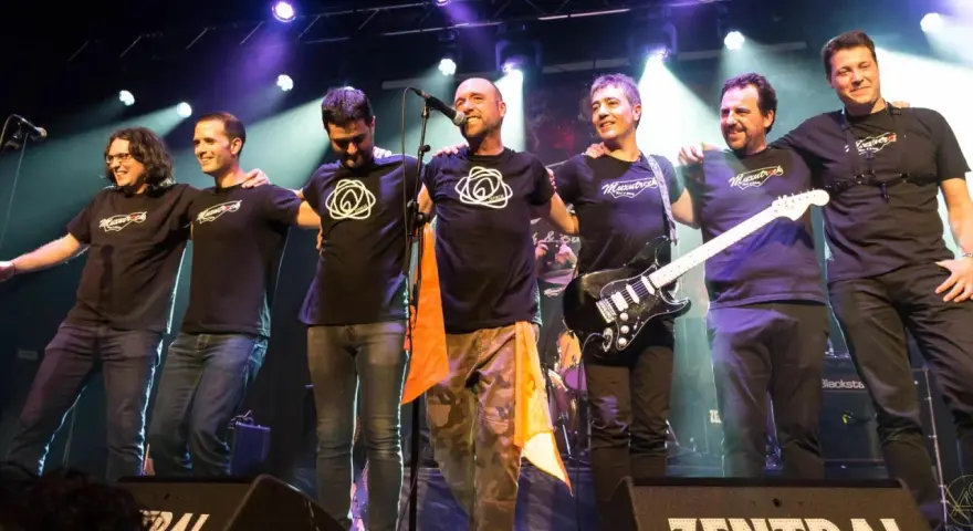 Seis músicos de maizu rock en el escenario, abrazados y sonriendo. Uno sostiene una guitarra eléctrica.