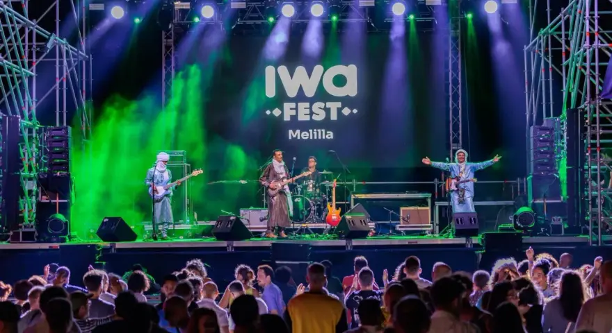 Banda tocando en el iwa fest de Melilla, con luces verdes y moradas, y una multitud disfrutando.
