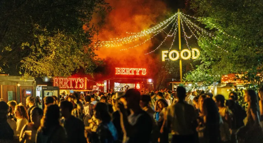 Noche de fiesta con luces de neón "Bertys" y "Food", gente disfrutando, ideal para canciones para un día ewan.