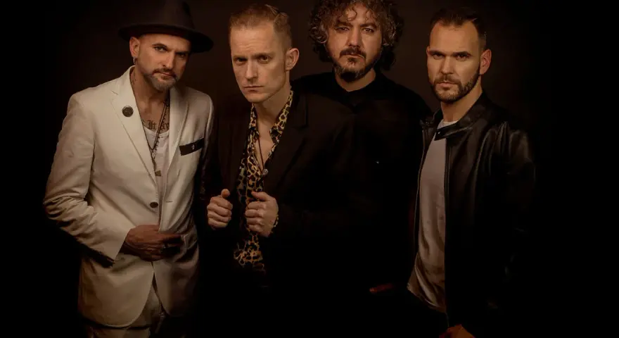 El grupo de embusteros posa con miradas intensas. Uno lleva sombrero y traje blanco, otro camisa de leopardo, y los otros dos, chaquetas oscuras.