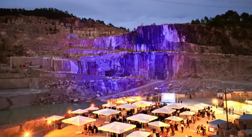Un impresionante festival Porriño ilumina una cantera con luces moradas. Gente reunida bajo sombrillas blancas, disfrutando del evento.