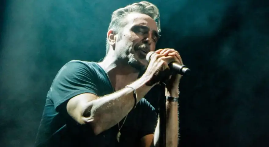 Un miembro de OBK canta apasionadamente en el escenario, iluminado por focos.