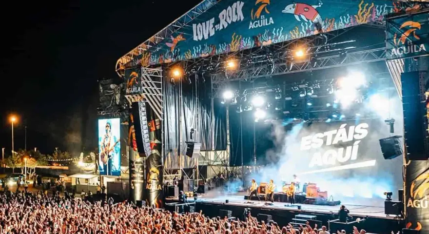 Multitud en concierto, luces brillantes y humo en el escenario. El cartel dice "Love to Rock".