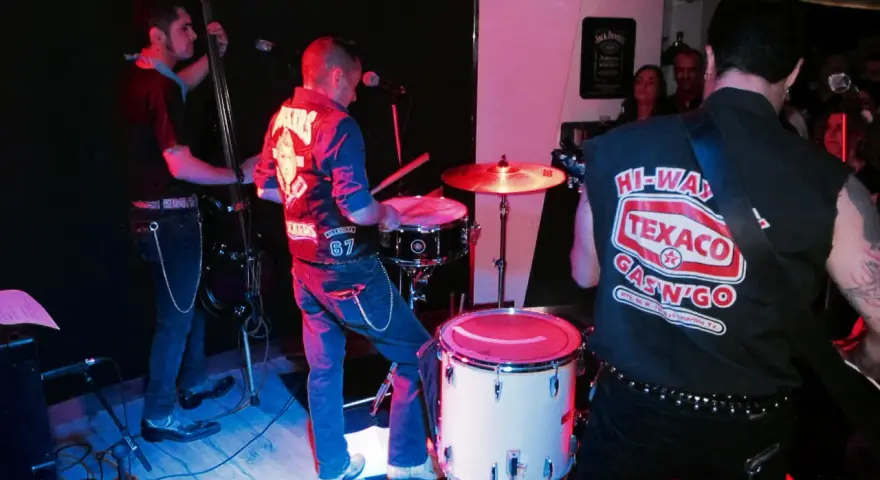 Un grupo de gatos locos en el escenario, tocando rock and roll con un contrabajo, batería y guitarra.