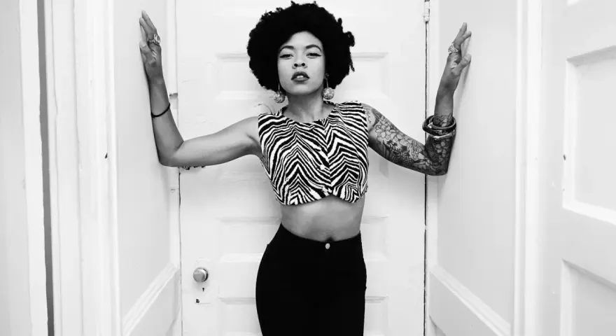 Nikki Hill, con su afro y top de cebra, posa con confianza entre puertas blancas.