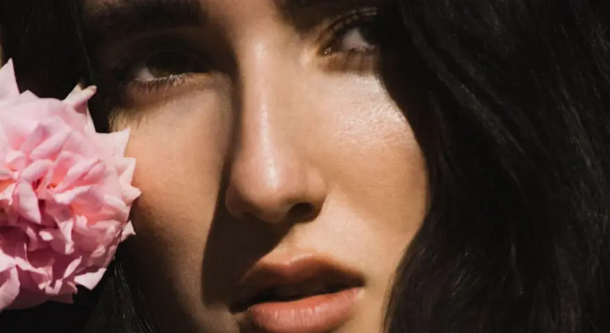 Primer plano de Judeline, cantante, con una flor rosa junto a su rostro.