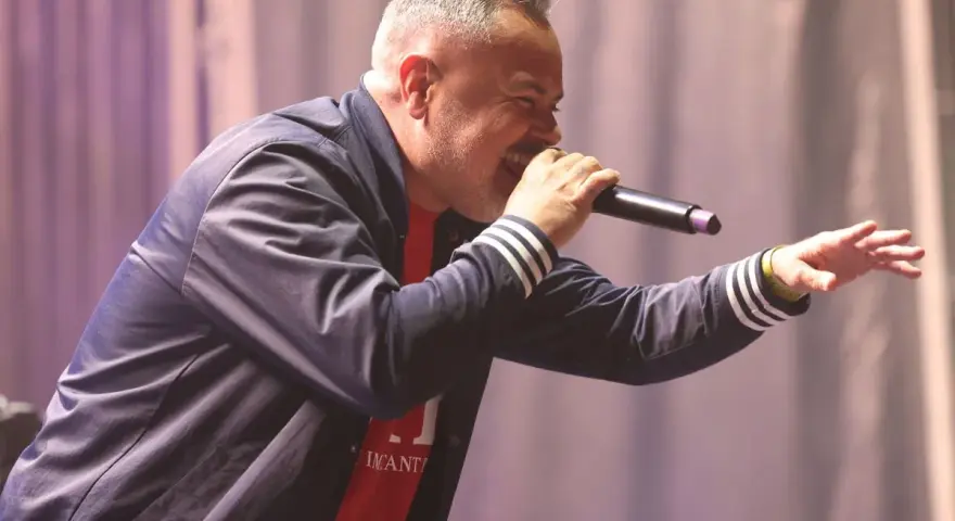 Juan Magán cantando en un escenario con micrófono y gesto animado.