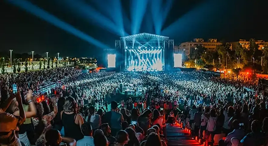 Gran concierto nocturno con multitud de público frente a un escenario iluminado con luces azules.