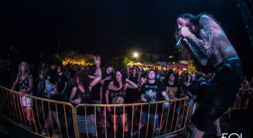 Un cantante con tatuajes canta en un concierto de charca rock. El público, animado, se agolpa tras una valla amarilla.