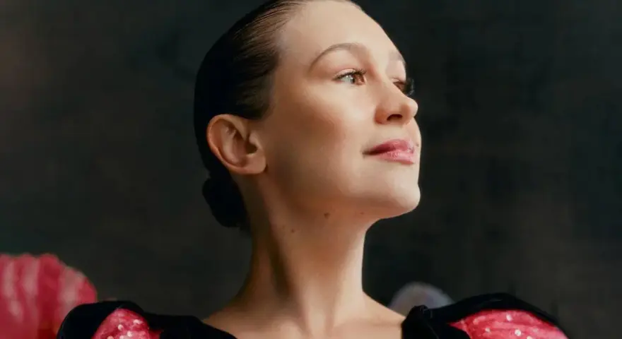 Joanna Newsom, con su cabello recogido y un vestido negro con detalles brillantes, mira hacia arriba con una expresión serena.