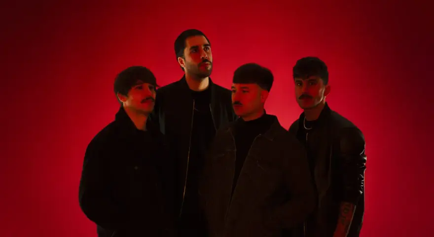 Cuatro hombres posan ante un fondo rojo vibrante. Parecen una banda, quizás "los flamingos", con sus miradas intensas y atuendos modernos.