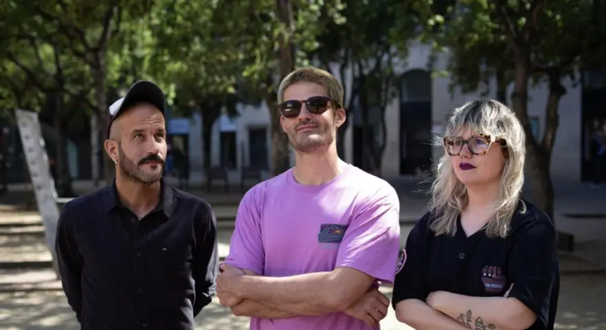 Miembros de Els Catarres posan al aire libre. El hombre de la izquierda lleva gorra y camisa negra. El del centro, gafas de sol y camiseta lila. La mujer de la derecha, gafas y camiseta negra.