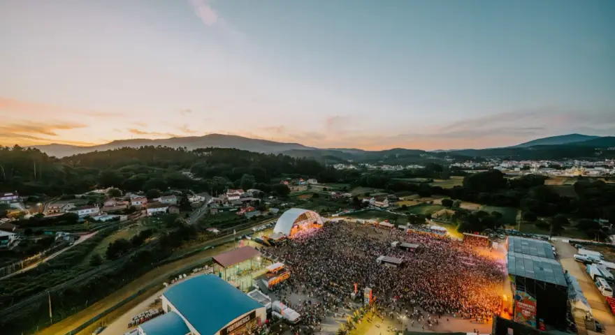 Multitudinaria **rio verbena fest** bajo un atardecer espectacular. Miles de personas disfrutan de la música y el ambiente.