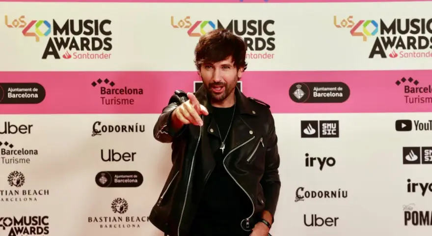 Hombre con chaqueta de cuero negro señala a la cámara en una alfombra roja de Los40 Music Awards. ¡Parece que ha pescado el premio!
