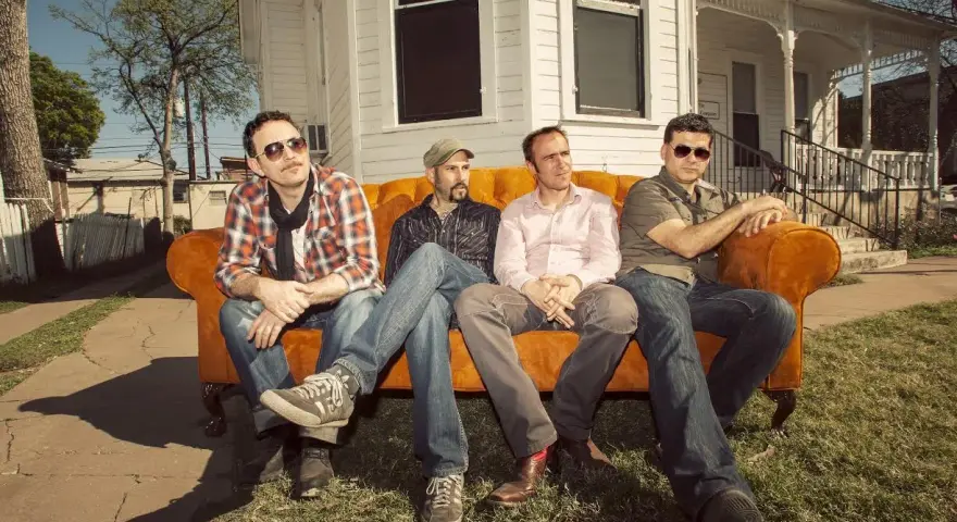 Cuatro hombres sentados en un sofá naranja, como si fueran **track dogs** esperando su próxima aventura.