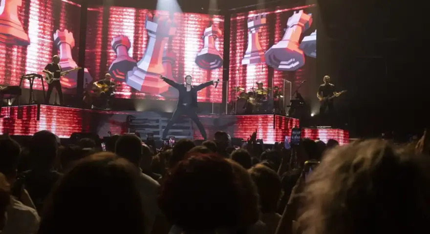 Un cantante en el escenario del 101 music festival, con una pantalla gigante de ajedrez de fondo.