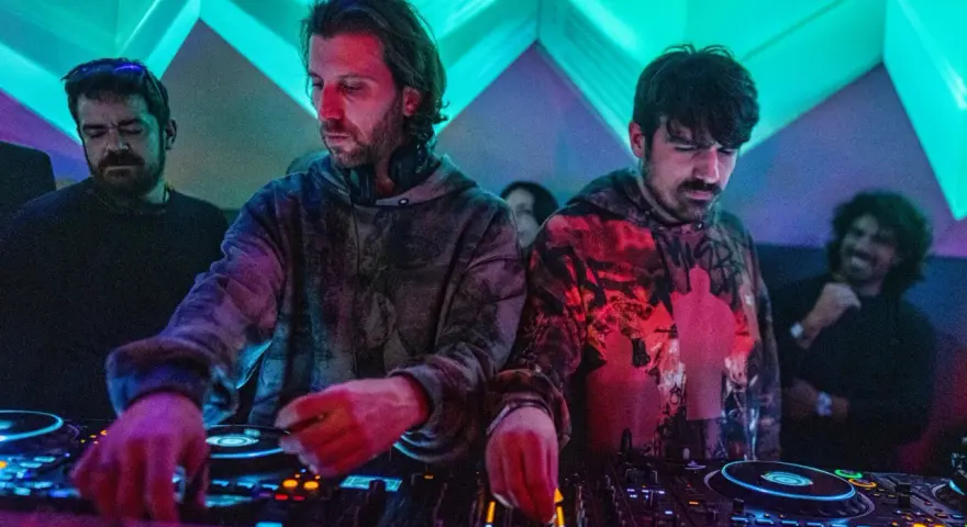 Los agentes del tiempo, DJs concentrados, manipulan las consolas bajo luces de neón, creando ritmos que desafían el tiempo.