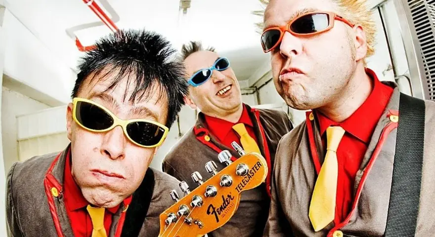 Tres músicos con gafas de sol y trajes coloridos, listos para un concierto de mondra roll.