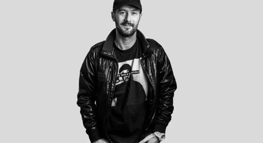 DJ Plan B, con gorra y chaqueta de cuero, sonríe con una camiseta que dice "Today was a good day".