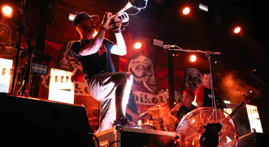 Músico con trompeta en un concierto de soria rock, con luces rojas y fondo de calaveras.