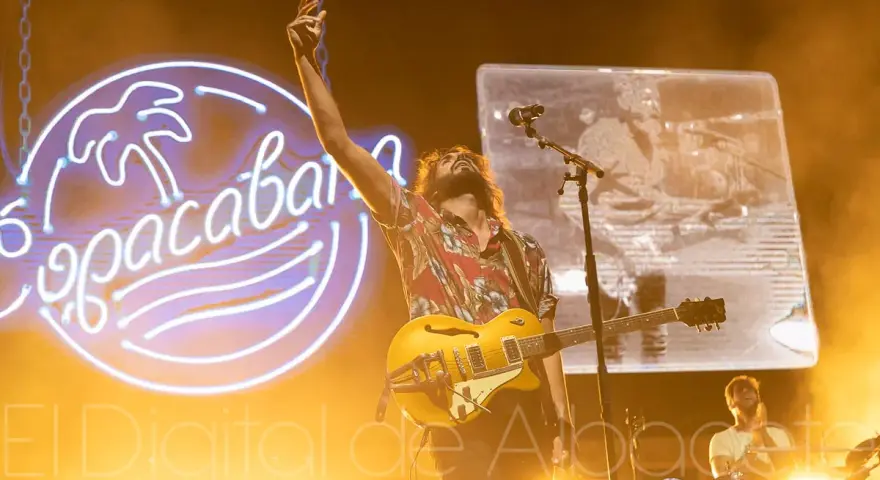 El cantante de Izal en Albacete levanta la mano con su guitarra amarilla, iluminado por un neón de Copacabana.