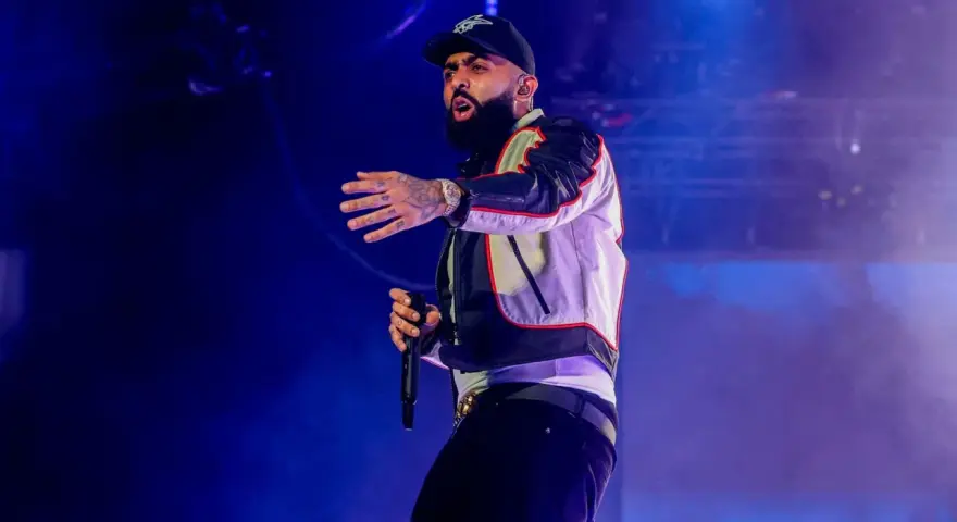 Nicky Jam, con su gorra y chaqueta llamativa, canta en un concierto en Granada, cautivando al público con su energía.