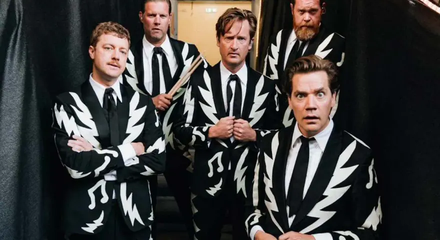 Los miembros de The Hives posan con trajes llamativos. Uno sostiene baquetas, listo para la acción.