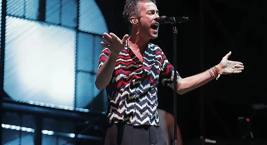 El cantante de Vetusta Morla Sevilla canta apasionadamente en un concierto, con las manos extendidas y un micrófono frente a él.
