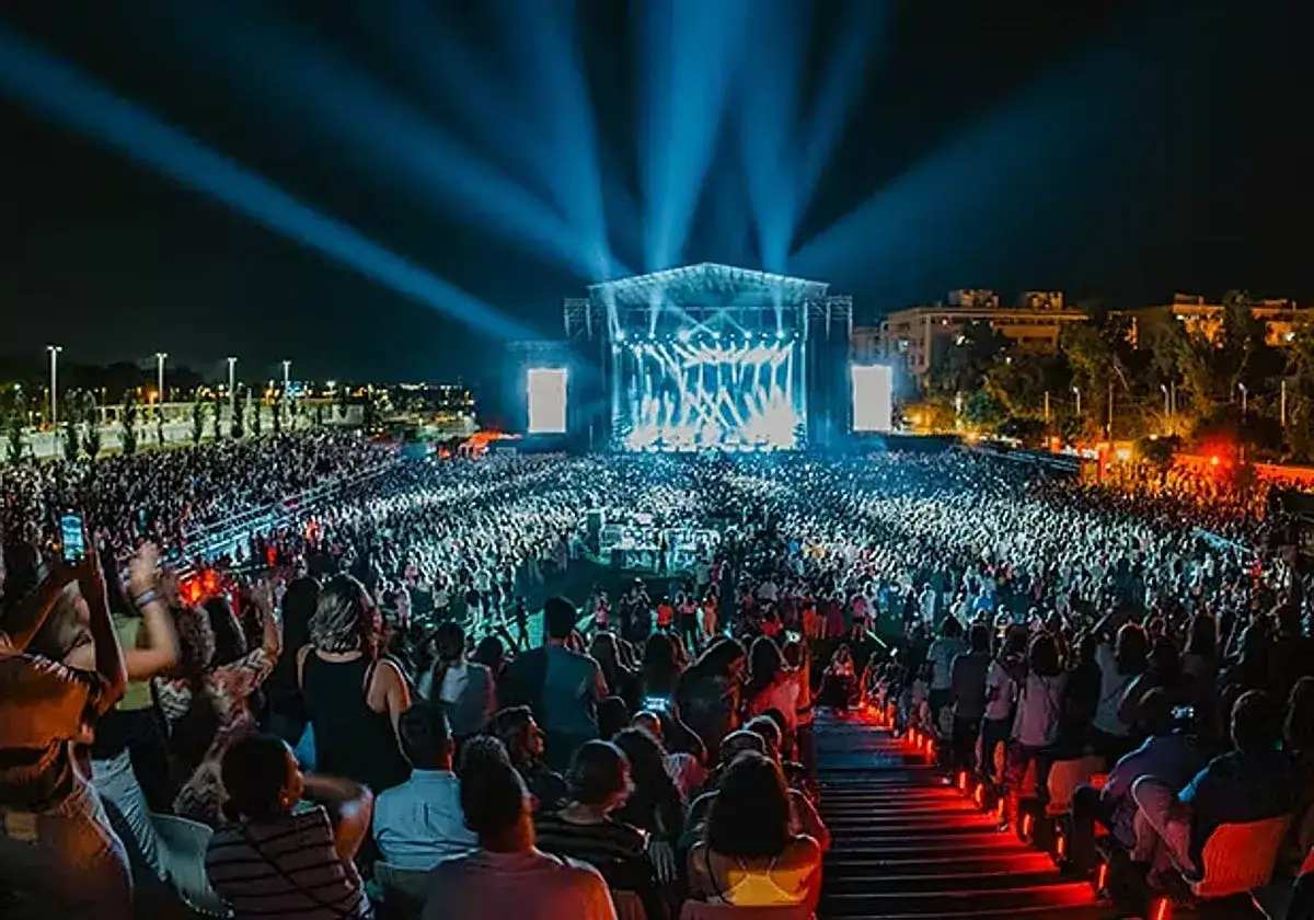 Multitud disfrutando de un concierto nocturno con luces espectaculares en el escenario. Un evento que evoca la magia del cabaret mairena.