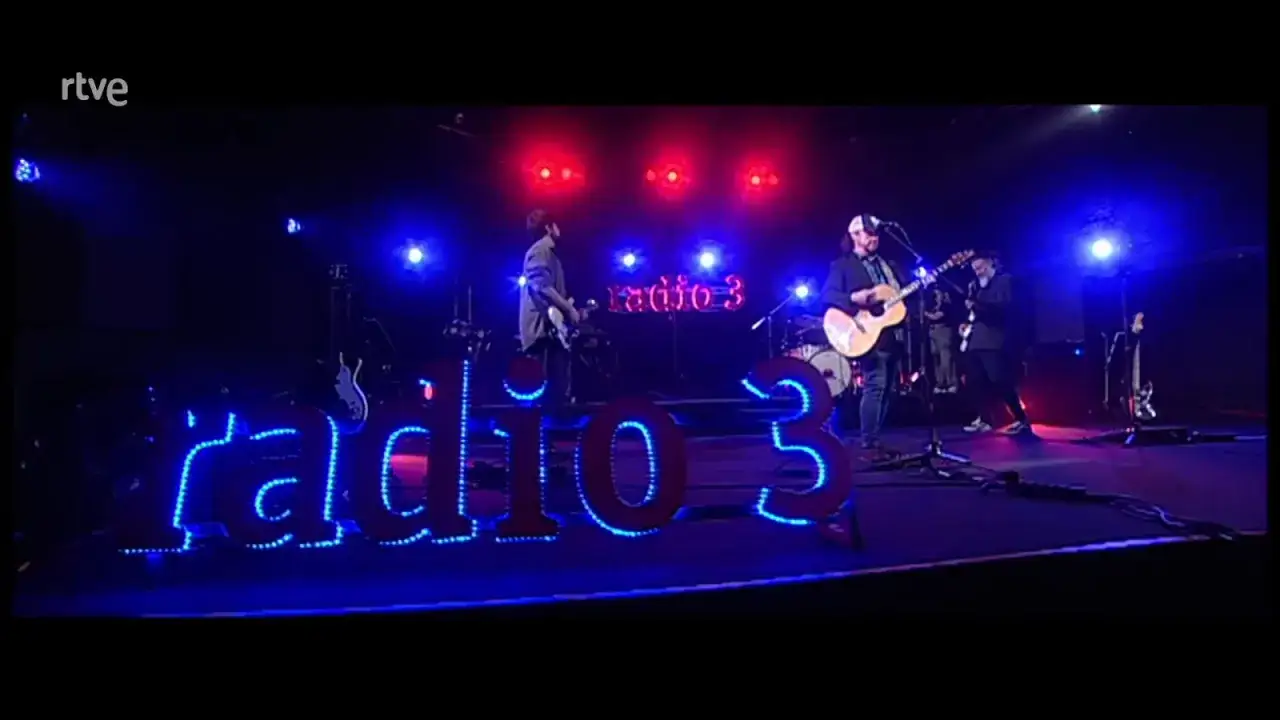 Luis Brea y su banda tocan en Radio 3, iluminados por luces rojas y azules.