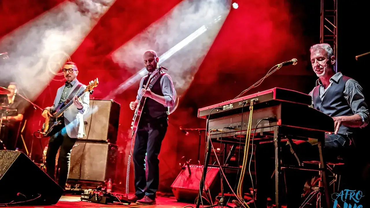 El grupo de parquesvr en concierto, con guitarrista, bajista y tecladista bajo luces rojas.