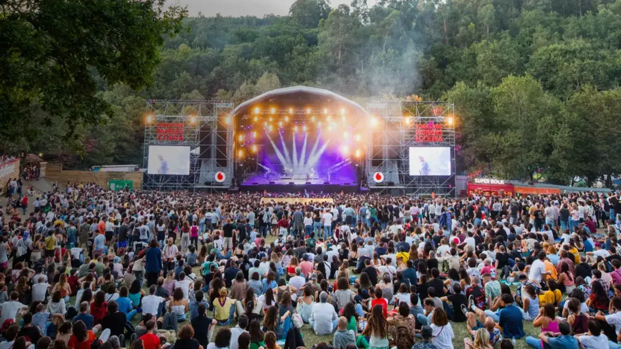 Multitud disfrutando del festival Paredes de Coura bajo un gran escenario iluminado.