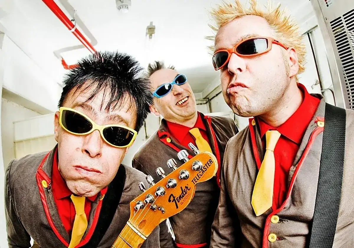Tres músicos con gafas de sol y trajes llamativos, listos para un concierto de mondra roll.