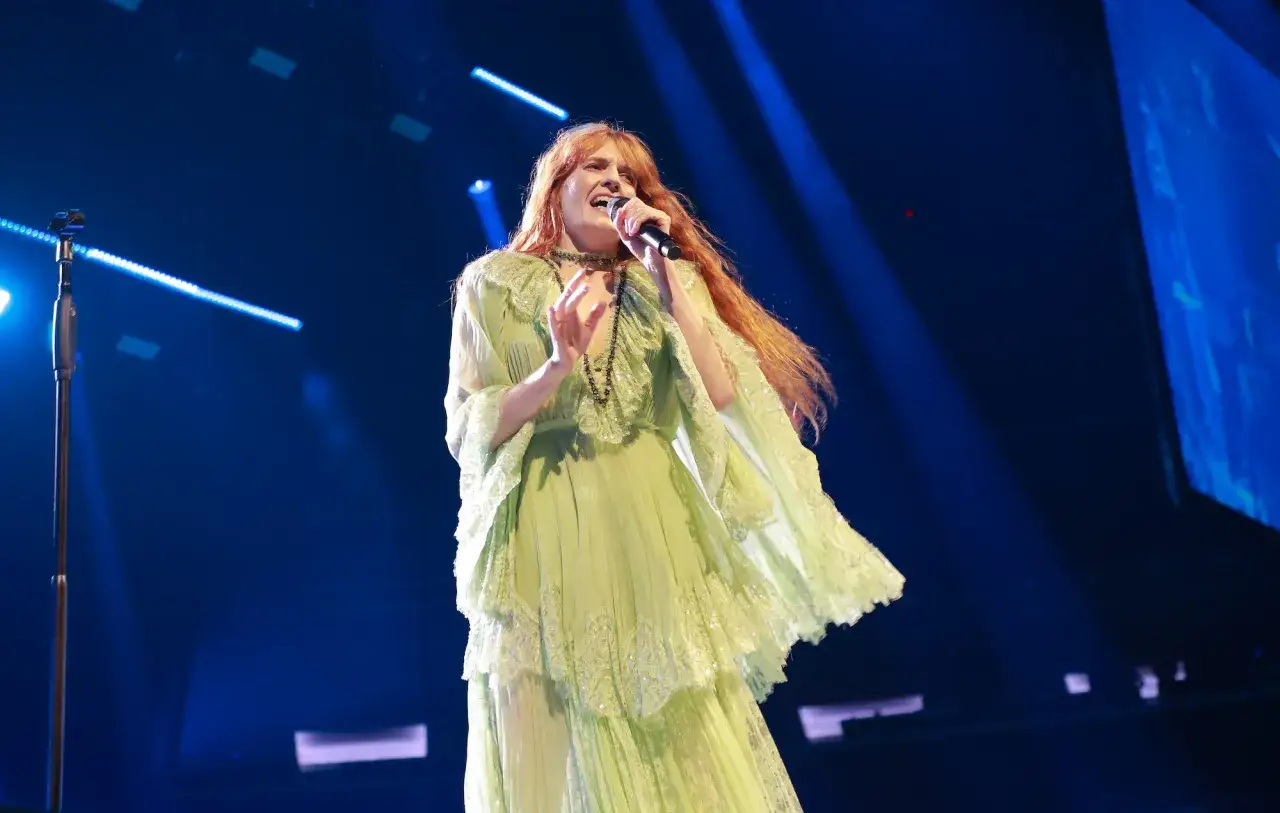 Florence Welch, una de los miembros de Florence and the Machine, canta apasionadamente en un escenario con luces azules.